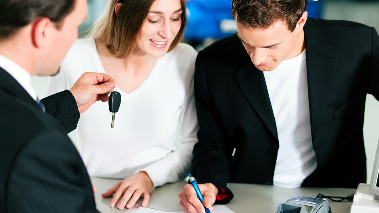 A man holding out keys to a man and woman looking over documents