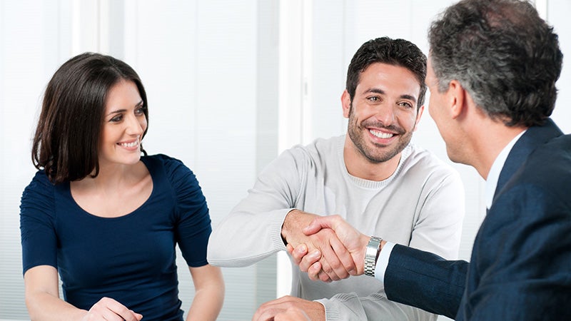 A woman watching a man shake hands with a car dealer
