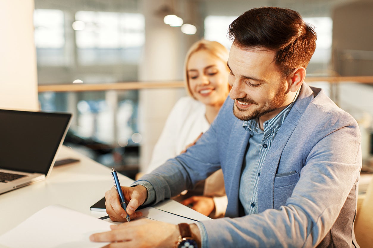 A man and woman signing paperwork at a dealership finance center